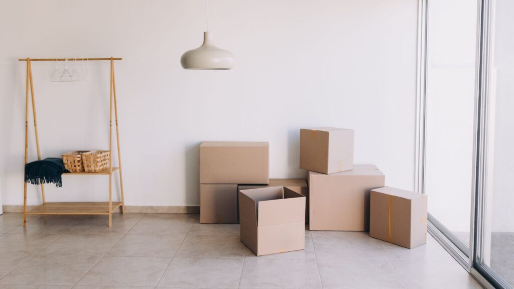 Minimalist room with stacked cardboard boxes, a wooden shelf, and pendant light, ideal for moving or home organization.